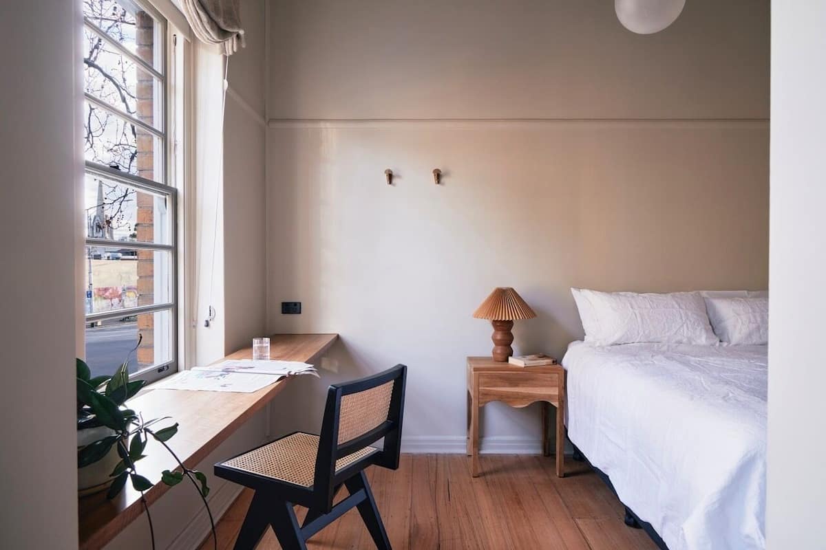 Un dormitorio con cama, un escritorio con silla, una lámpara y una ventana.