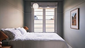 Ein Schlafzimmer mit einem großen Bett, einem Fenster mit Ausblick und einem gerahmten Bild an der Wand.