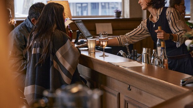 Eine Bar mit einer Holztresen, einem Laptop sowie verschiedenen Flaschen und Gläsern.