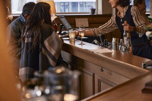 Una zona de bar con mostrador de madera, una computadora portátil y diversas botellas y vasos.