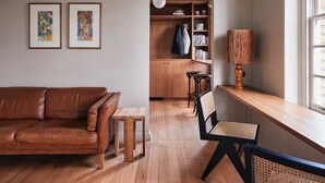 Ein gemütliches Wohnzimmer mit einer braunen Ledersofa, einem Holztisch und einem Essbereich mit Holztisch und Stühlen. Ein Bücherregal voller Bücher und eine Hängeleuchte sind ebenfalls vorhanden.