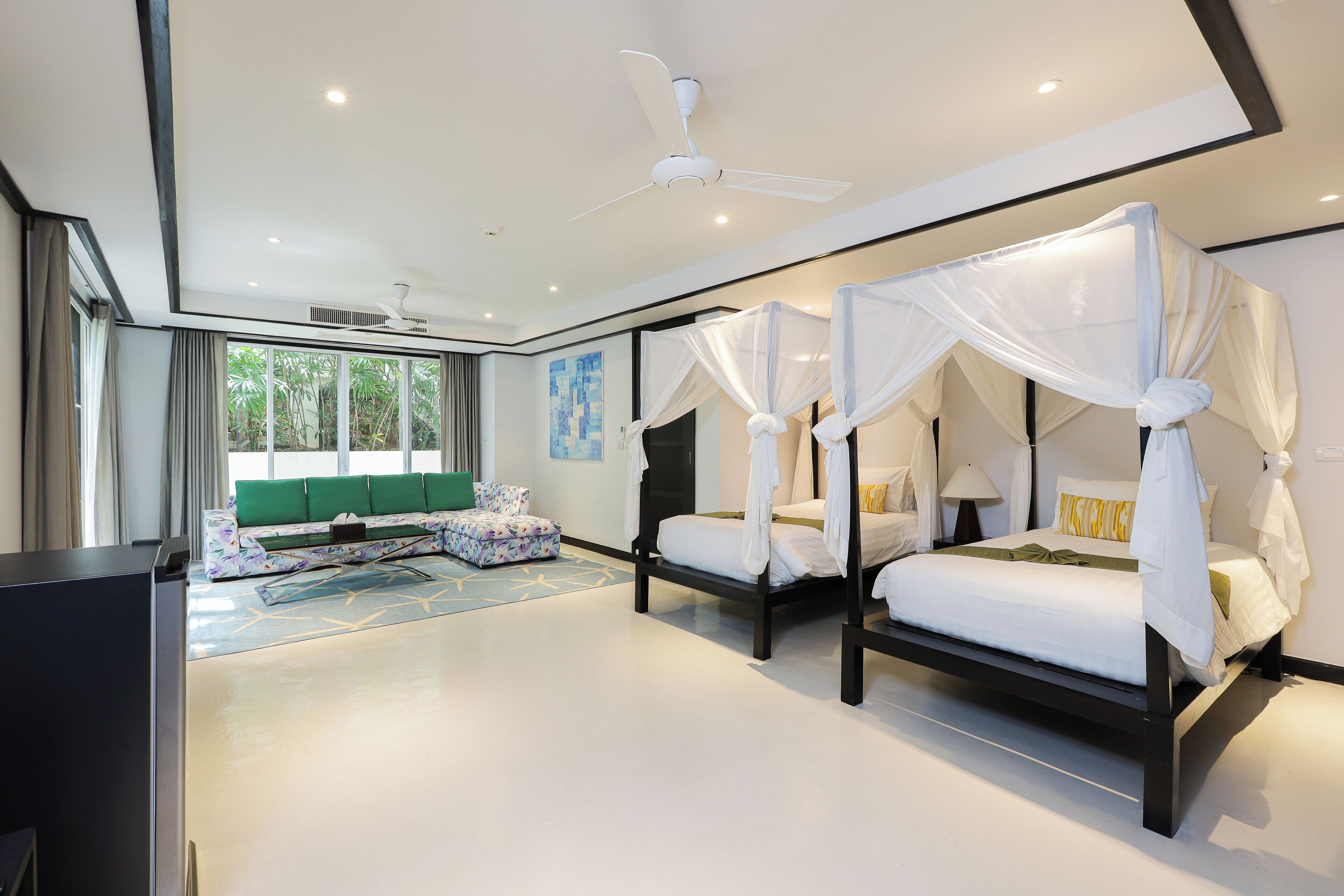 A modern bedroom with two beds, a green sofa, and a large window.