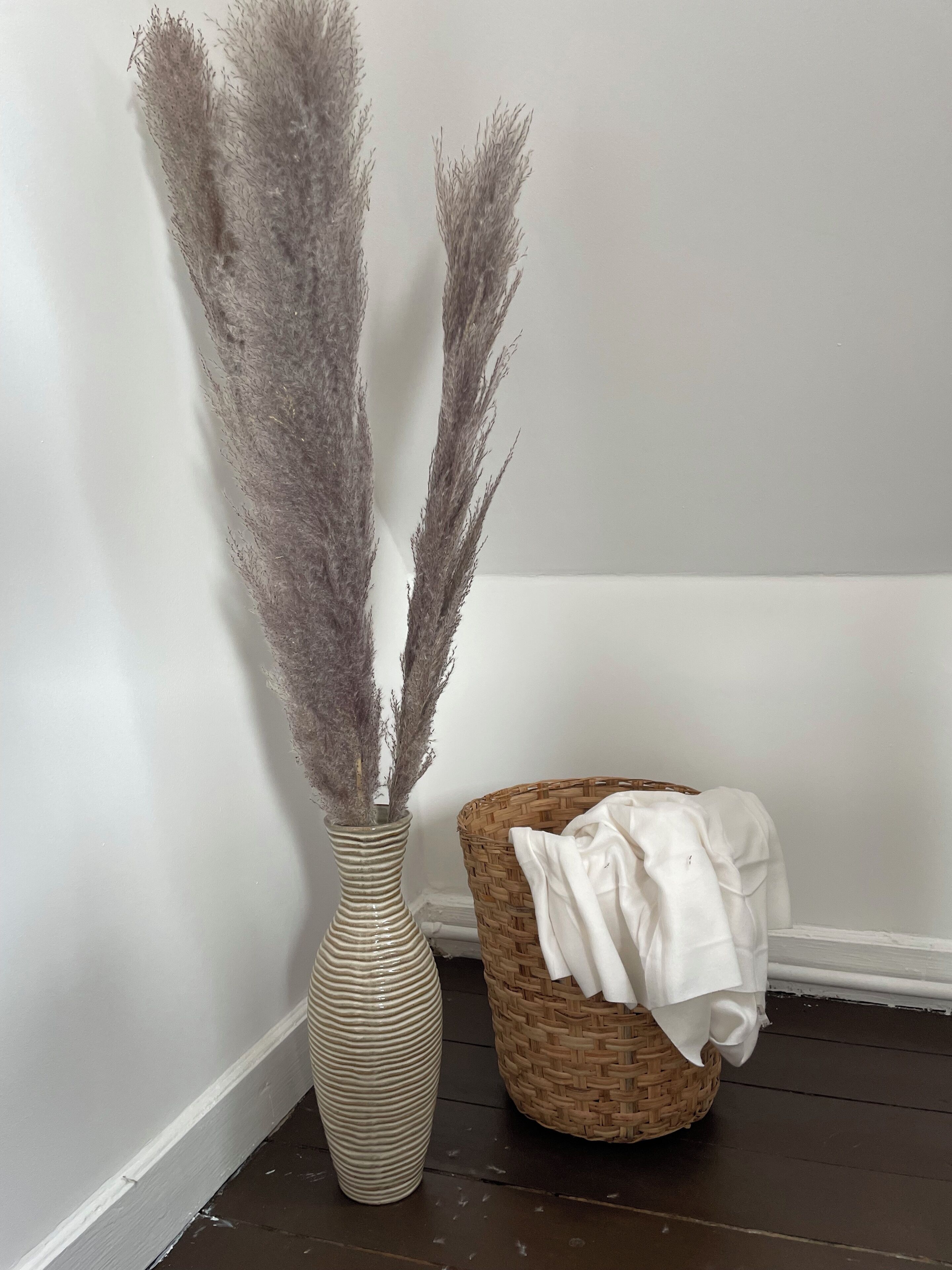 A vase with dried pampas grass and a wicker basket with a white cloth.