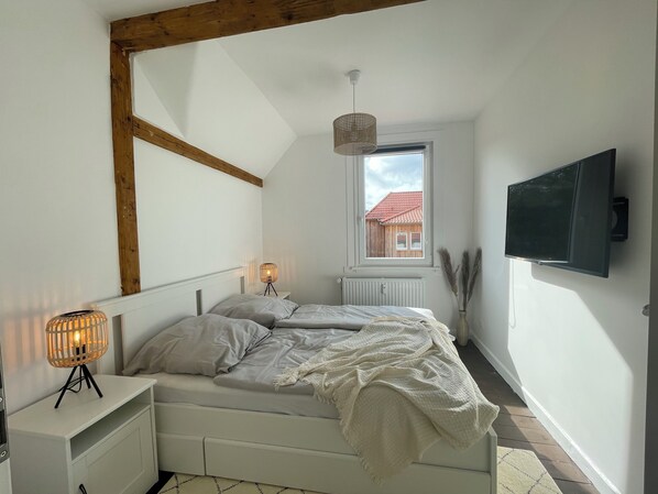 Ein Schlafzimmer mit Bett, Nachttisch, Lampe, Fenster und Fernseher.