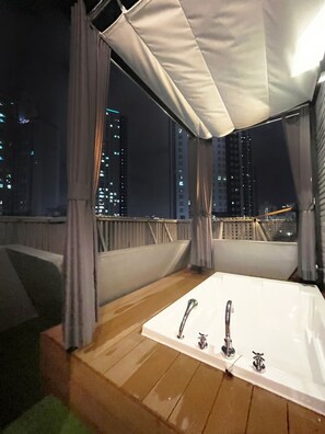 A rooftop terrace with a hot tub, curtains, and a city view at night. - The van stay (Busan)