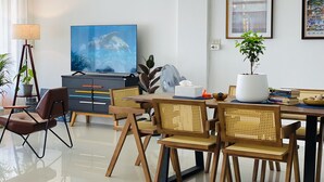 Un soggiorno moderno con una TV a schermo piatto, un tavolo da pranzo con sedie, una lampada da terra e una pianta in vaso.
