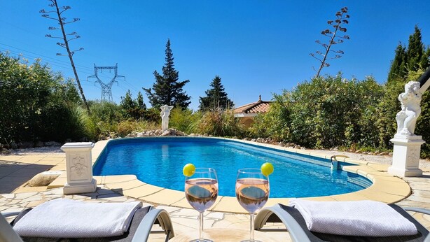 A poolside area with two lounge chairs, a table with two glasses of wine, and a statue in the background. - Beautiful southern villa with private pool (Oupia)