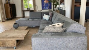 A modern living room with a grey sectional sofa, a wooden coffee table, and a large window with curtains. - Beautiful southern villa with private pool (Oupia)