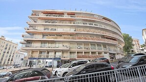 Un edificio de varios pisos con balcones, un estacionamiento y otros edificios al fondo.