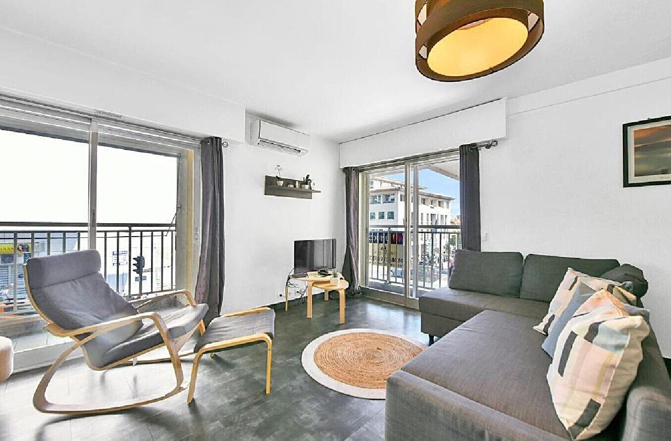 Un salon moderne comprenant un canapé, un fauteuil à bascule, un téléviseur et une grande fenêtre donnant sur des immeubles.