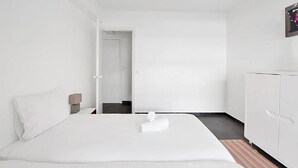 Una habitación de hotel con una cama, una mesita de noche, un armario y una puerta que da a otra habitación.
