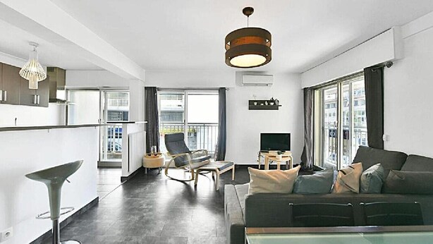 Una sala de estar moderna con un sofá, una mesa de comedor y un televisor. Hay un balcón con una silla y una ventana.