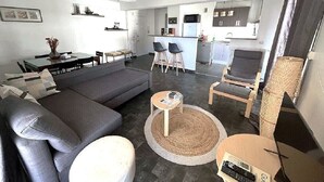 Una sala de estar moderna con un sofá gris, una mesa redonda de centro y un comedor con una mesa pequeña y sillas.