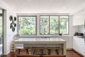 Una cucina moderna con un'isola grande, mobili bianchi e ampie finestre che danno su un'area verde.