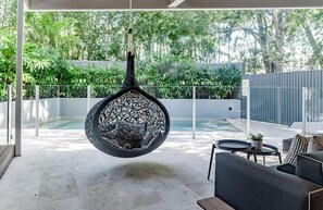 A modern outdoor seating area with a hanging chair, a sofa, and a small table with a plant.