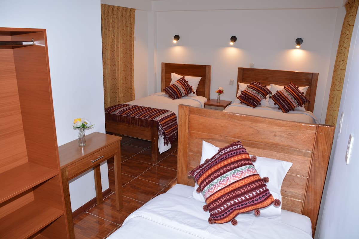 A hotel room with two wooden beds, each with patterned pillows and headboards, a wooden nightstand with a vase of flowers, and a wooden desk.