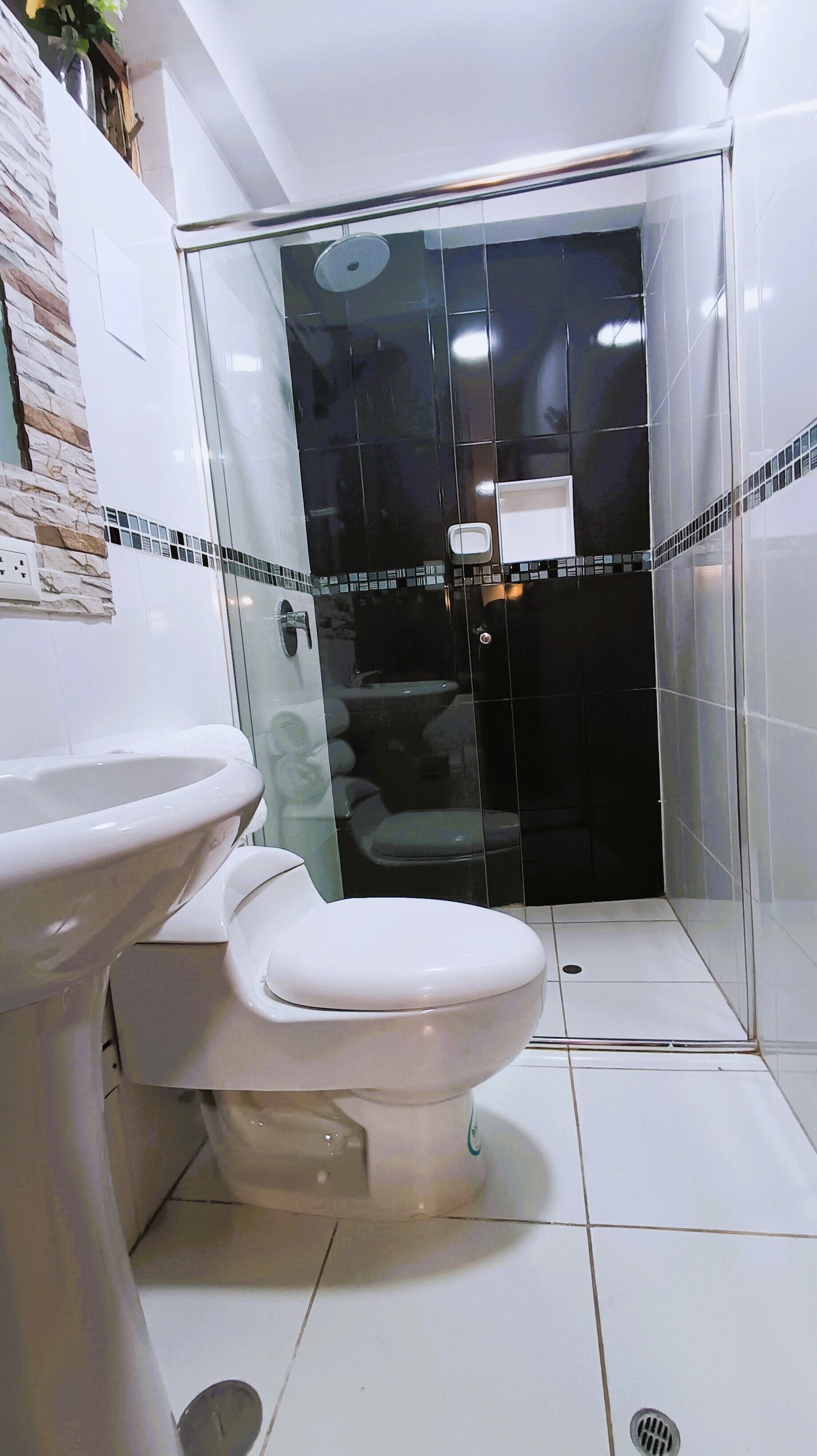 Een badkamer met een wit toilet, een douche met glazen wanden en een betegelde vloer.