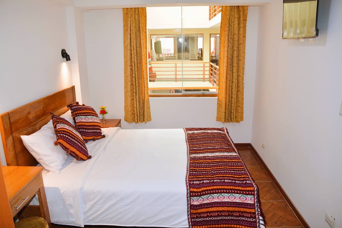 A hotel room with a bed, a nightstand, a window with curtains, and a view of an outdoor balcony.