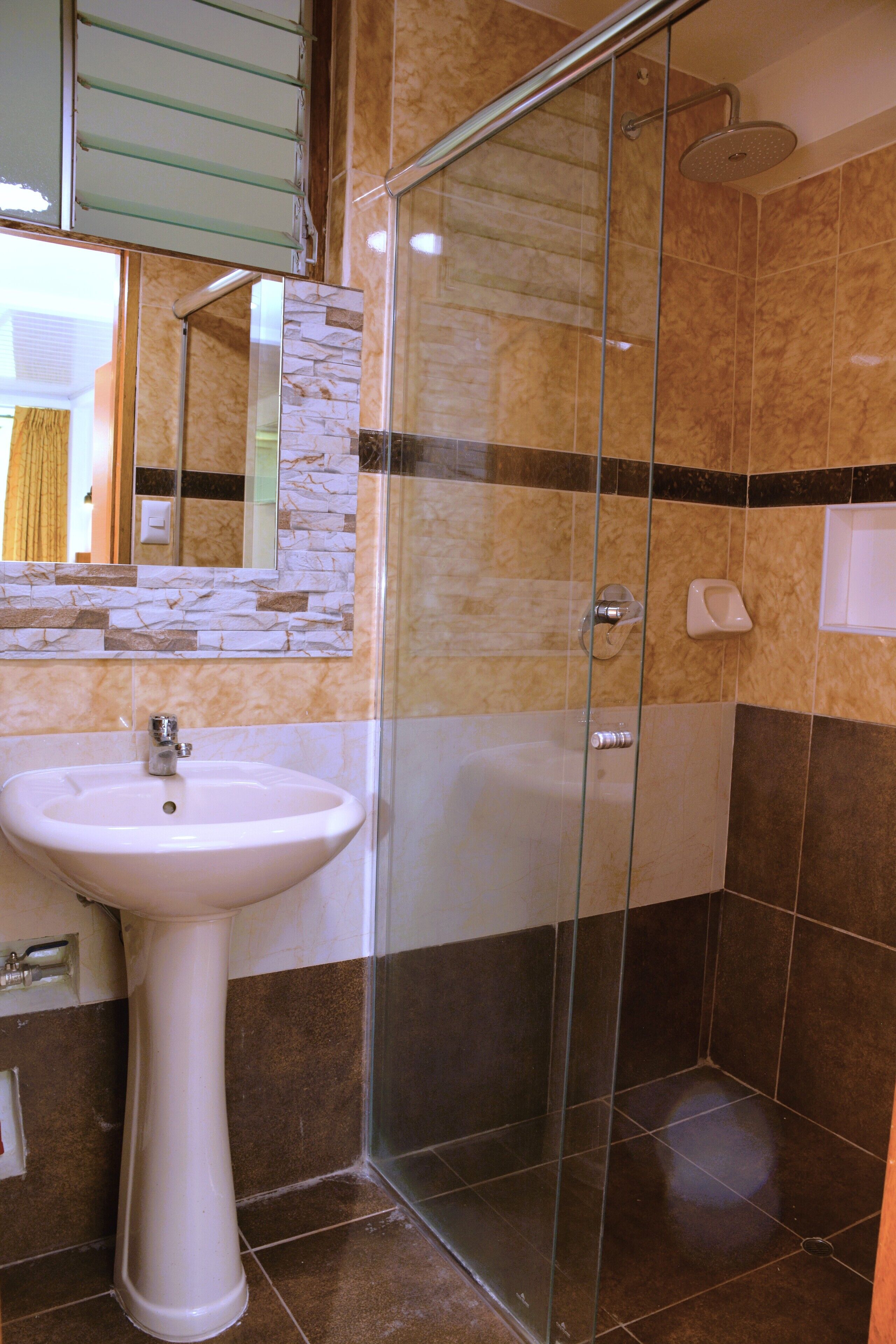 A bathroom with a glass-enclosed shower, a pedestal sink, and a mirror with a stone backsplash.