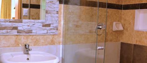 A bathroom with a glass-enclosed shower, a pedestal sink, and a mirror with a stone backsplash.
