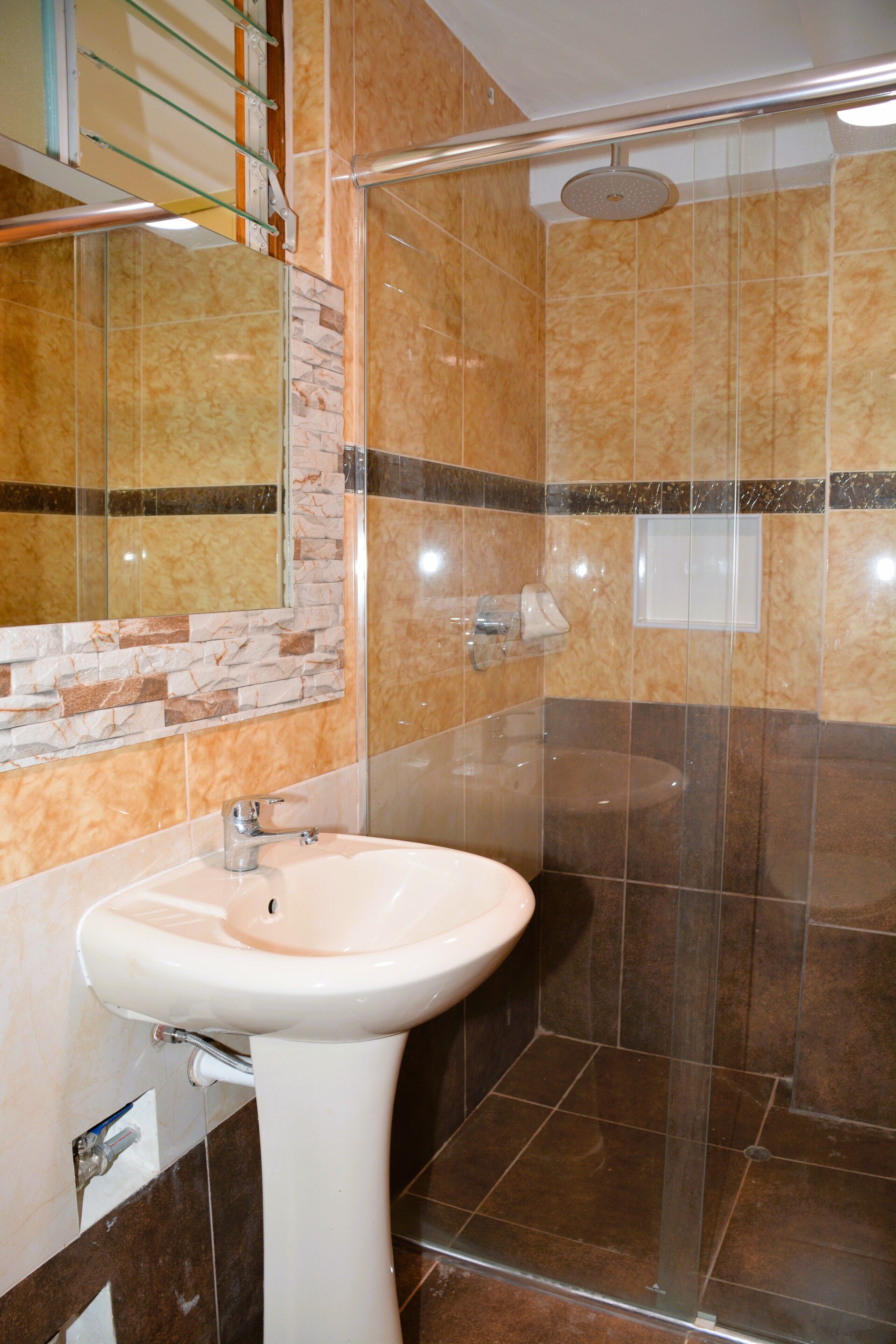 A bathroom with a marble sink, a glass shower enclosure, and a mirror with a stone backsplash.