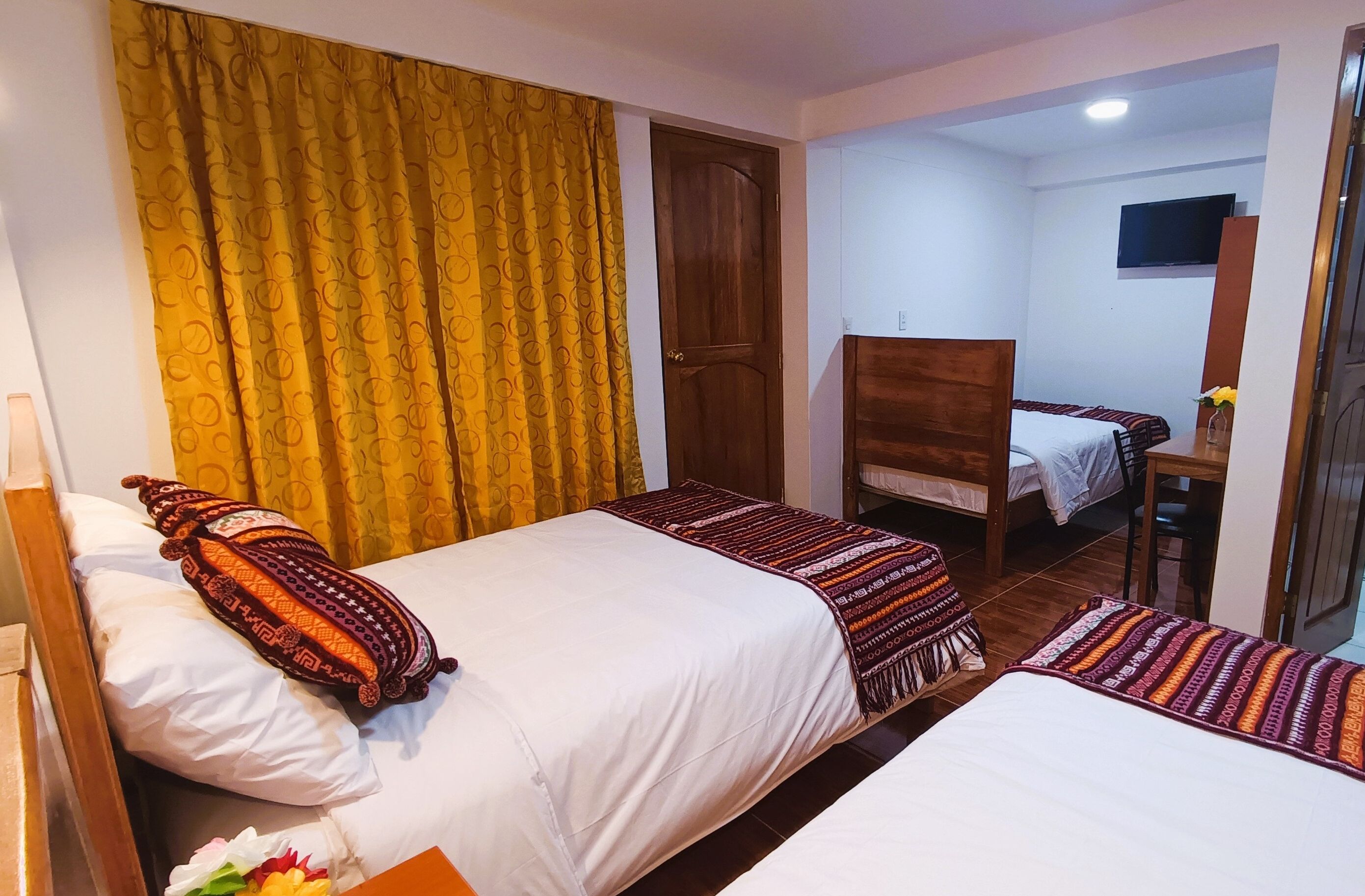 Une chambre d’hôtel avec deux lits, un bureau en bois, une télévision et une porte.