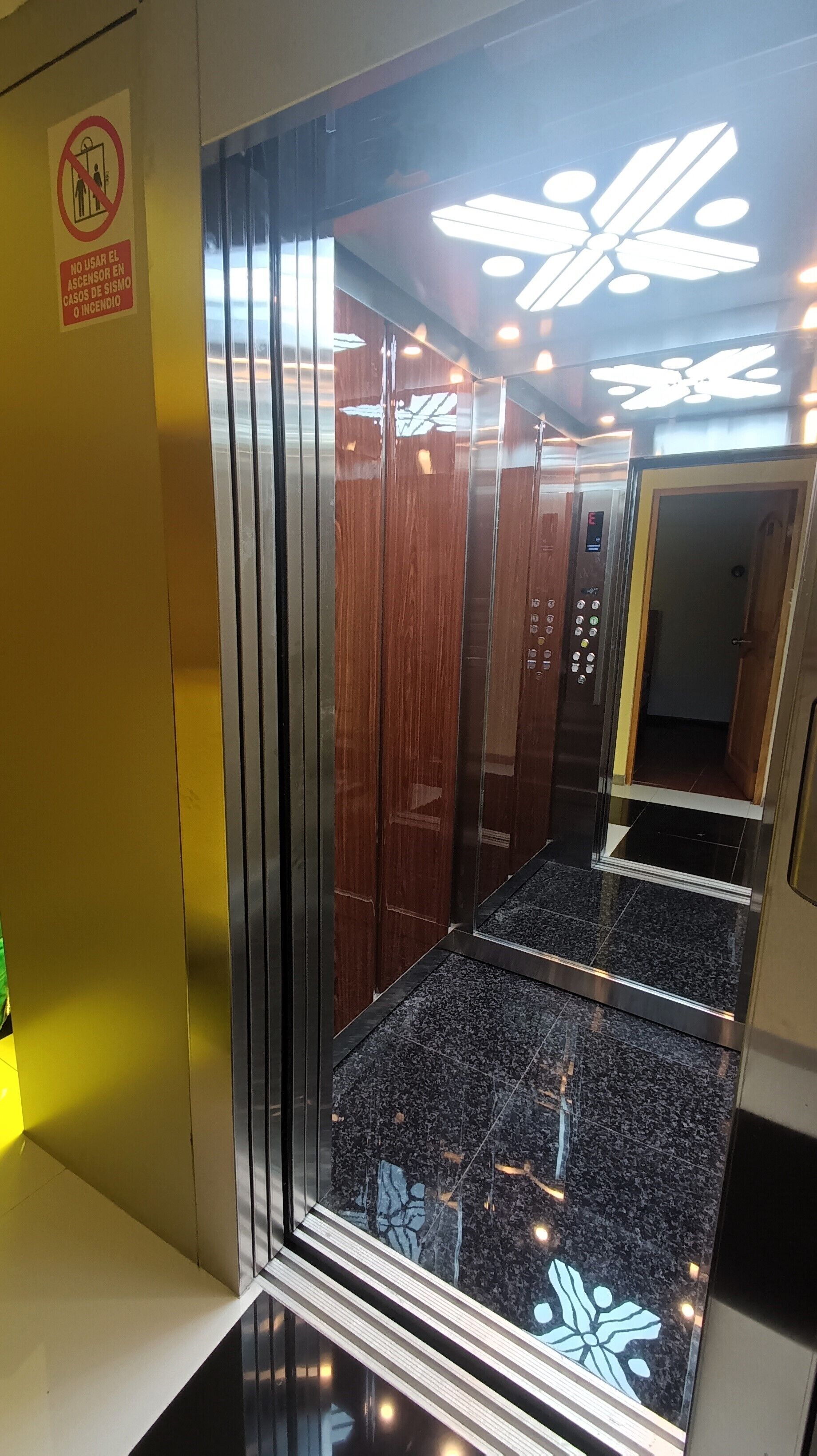 An elevator interior with a reflective floor, wooden panels, and a control panel.