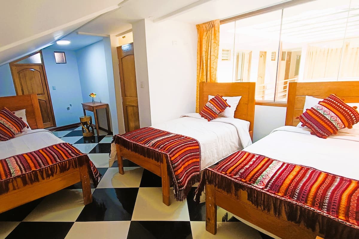 A hotel room with two beds, a small table, and a window with curtains.