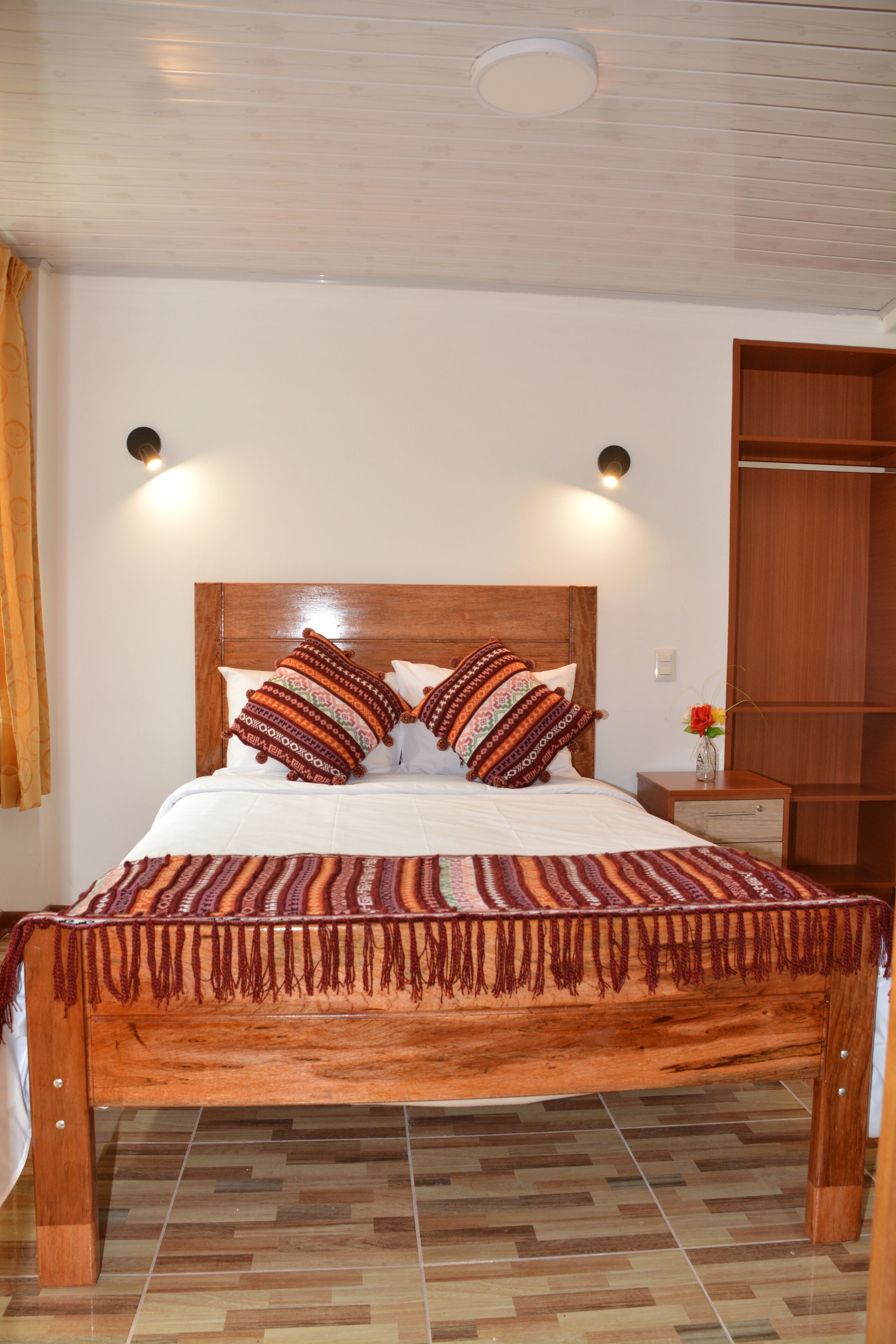 Una camera da letto con un letto di legno, cuscini decorati, un comodino con un vaso e un armadio.
