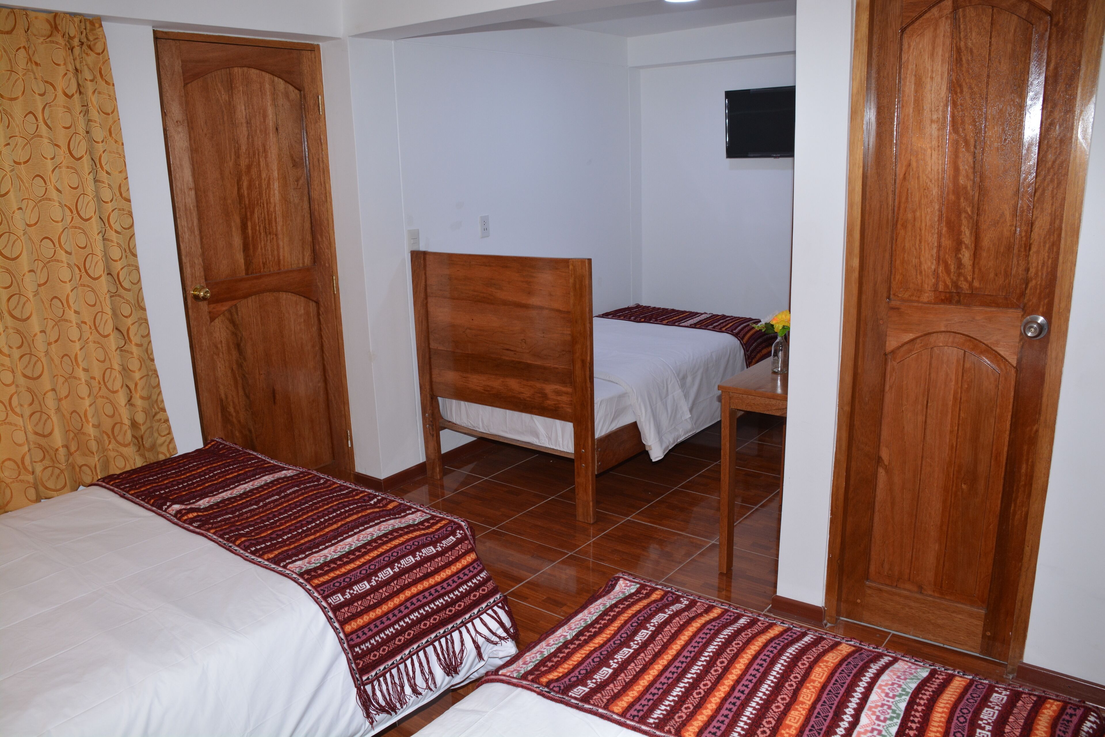 A room with two beds, a wooden chair, a small table with a vase, and patterned curtains.