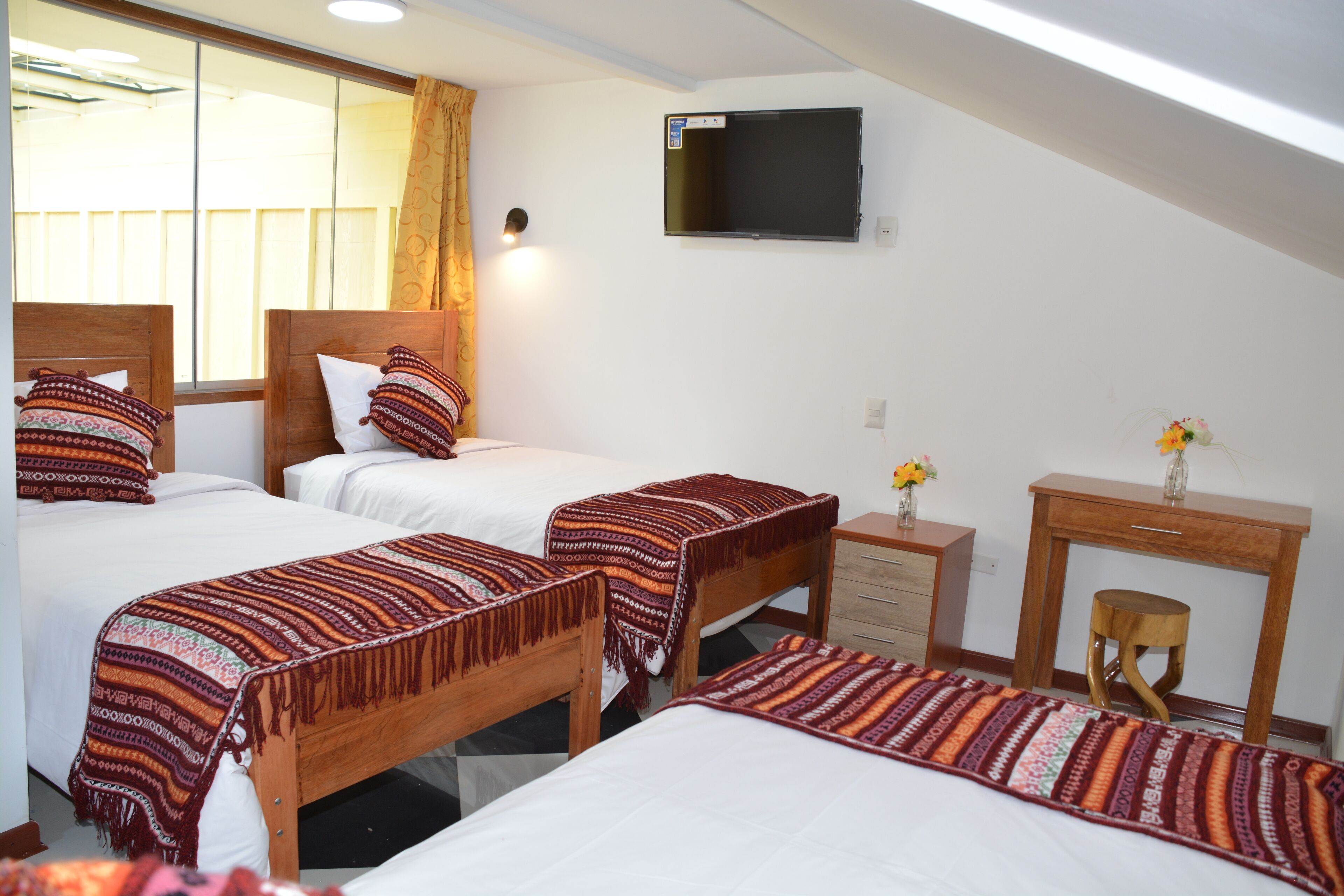 A hotel room with two beds, a TV, a wooden desk, and a small stool.
