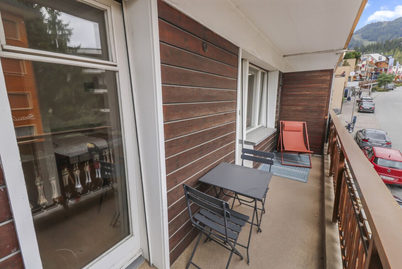 Ein Balkon mit Tisch und Stühlen, ein Fenster mit Blick auf die Straße und eine Holzwand.