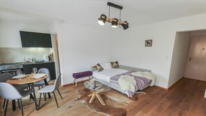 A compact living space with a dining area, kitchenette, and a bed with a fur throw. - Elegant studio in the heart of Crans (Crans-Montana)