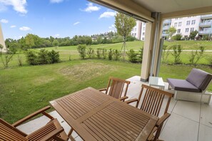 Guests can enjoy a patio with a table, chairs, and a sofa, surrounded by a lush lawn and trees.