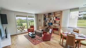 Een ruime woonkamer met een bank, fauteuils, een salontafel en een eethoek met stoelen en een gedekte tafel.