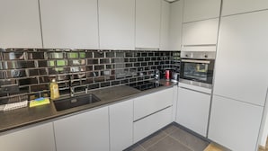Een moderne keuken met witte kastjes, een zwart betegelde achterwand en roestvrijstalen apparatuur.