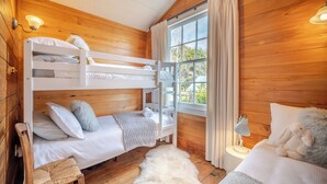 Une pièce de cabane en bois avec des lits superposés, une chaise, une lampe et une grande fenêtre avec des rideaux.