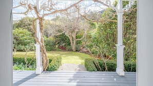 Une terrasse en bois couverte, agrémentée d’une pergola blanche, entourée d’une végétation luxuriante et d’un jardin bien entretenu.