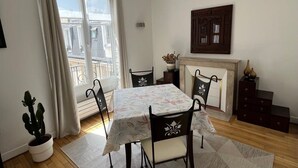 A dining area with a table set for four, a potted plant, and a view of a balcony. - Appartement Saint Antoine CityCosy (Paris)
