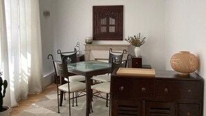 A dining area with a glass-top table, dark chairs, a wooden cabinet, and a decorative wall piece. - Appartement Saint Antoine CityCosy (Paris)