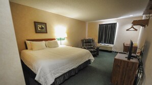 A hotel room with a large bed, a chair, a desk with a computer, a window with curtains, and a picture on the wall. - Hotel room with ONE KING BED (Yuma)
