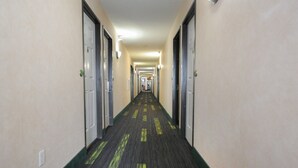 A long, narrow hotel corridor with doors on both sides and a carpeted floor. - Hotel room with ONE KING BED (Yuma)