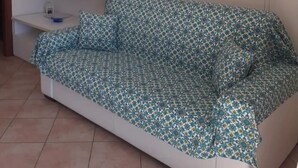 Uma sala de estar com um sofá estampado, um armário branco e um relógio de parede.