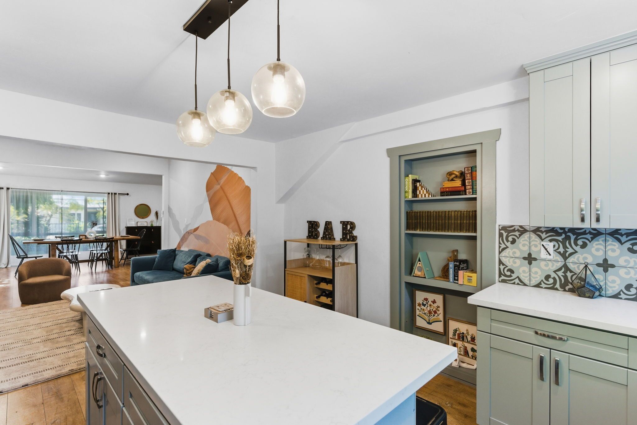 A modern kitchen with a central island, pendant lighting, and a dining area with a sofa and chairs.
