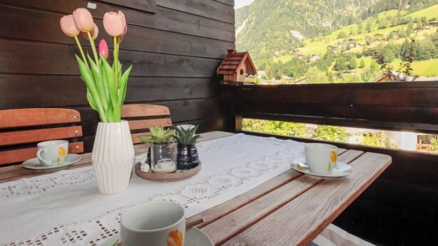 Eine Holzhütte mit gedecktem Tisch für zwei, einer Vase mit Tulpen und Blick auf ein grünes Tal.
