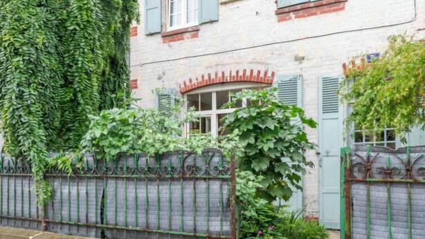 Un bâtiment de style européen traditionnel, avec une façade en briques, des volets verts et un portail en métal.