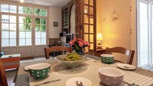 Un coin repas avec une table dressée pour quatre personnes, agrémentée d’une nappe à rayures, de bols verts et roses à pois et d’un saladier de raisins verts.