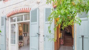 Un bâtiment rustique avec un escalier en bois menant à une porte, un petit espace extérieur aménagé pour s’asseoir et un sol carrelé.