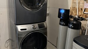 A stacked washer and dryer unit with a control panel, two water softeners, and visible plumbing. - Modern Private Suite in a serene location 15 minutes away from the Airport. (Airdrie)