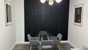 A modern dining area with a round glass table, grey upholstered chairs, and a black curtain backdrop. - Modern Private Suite in a serene location 15 minutes away from the Airport. (Airdrie)